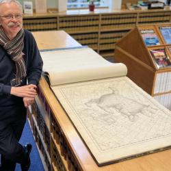 man looking at large star atlas in library